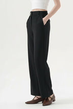 Black straight-leg trousers with a pleated waist, styled on the model